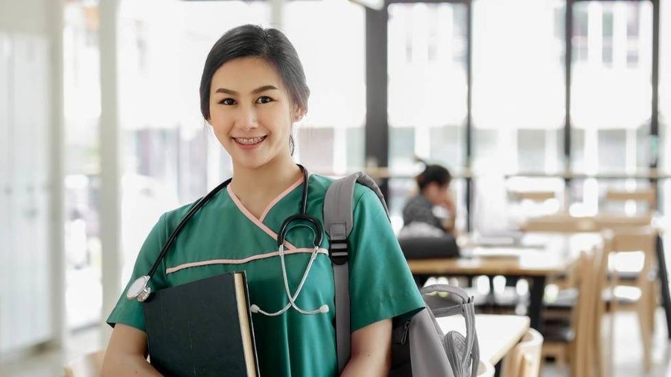 Student in green scrubs holding books in study hall