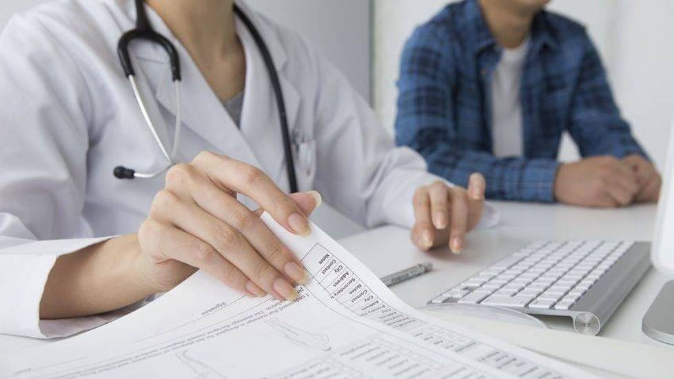 Doctor in lab coat looking at forms and computer