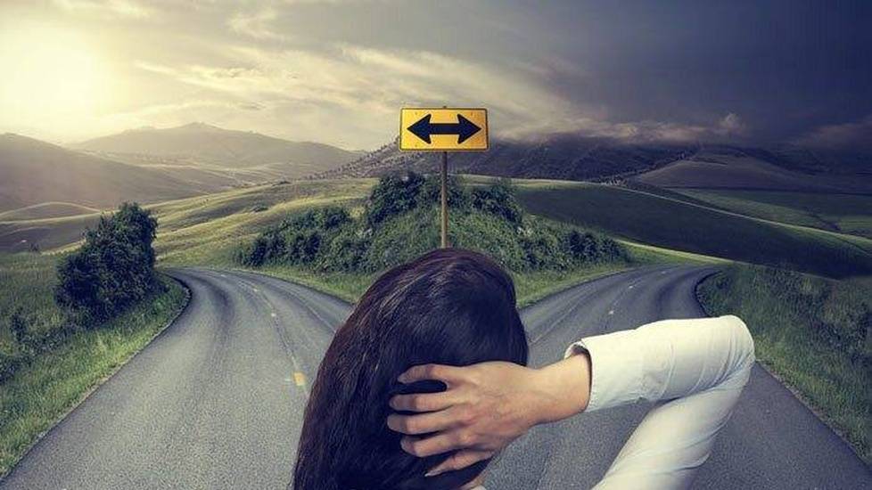 Woman at crossroads holding back of head thinking